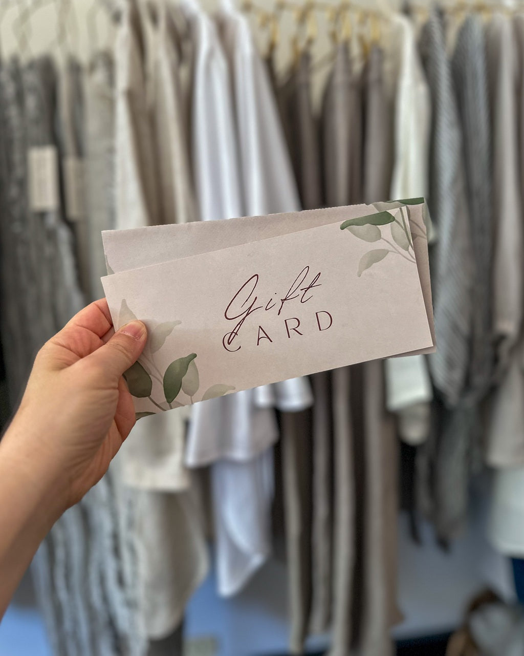 Hand holding a gift card with floral design in front of clothing racks